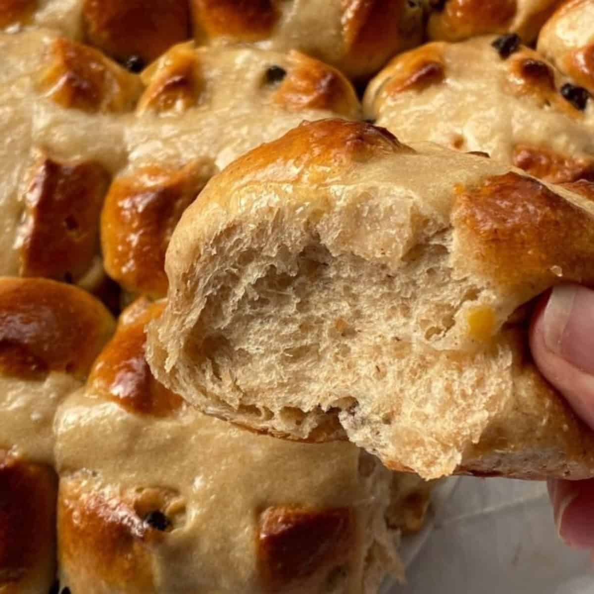 Hand holding a hot cross bun with fruit.