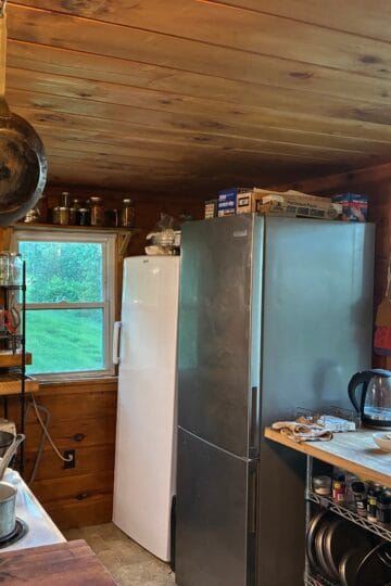 Rustic wooden kitchen with stainless steel fridge and hanging cast iron skillet, cosy country cooking space.