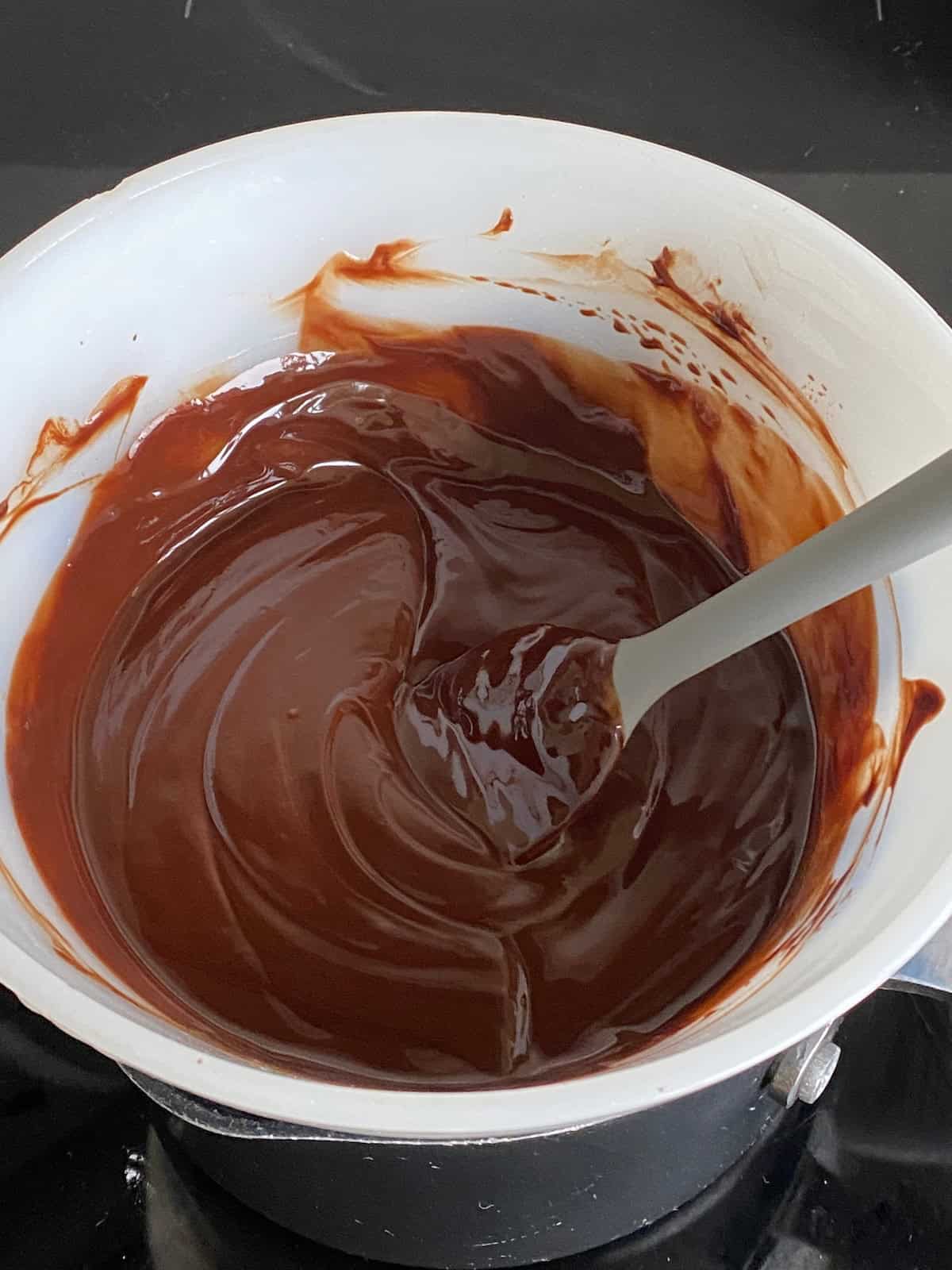 Melted chocolate in a dish and spread over a cake. Chocolate glaze in a white bowl.