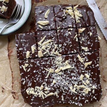 Rich chocolate brownie topped with white chocolate shavings and flakes, served on brown parchment paper, perfect for dessert lovers and chocolate enthusiasts.