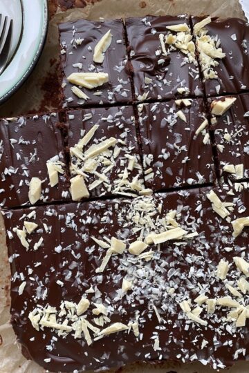 Rich chocolate brownie topped with white chocolate shavings and flakes, served on brown parchment paper, perfect for dessert lovers and chocolate enthusiasts.