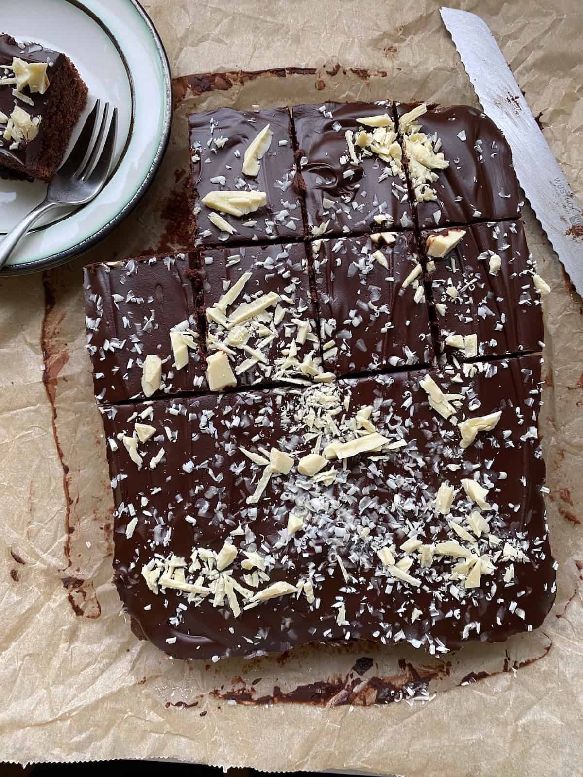 Chocolate Traybake Cake with a slice cut out. Chocolate traybake with a chocolate glaze and sprinkles of white chocolate.
