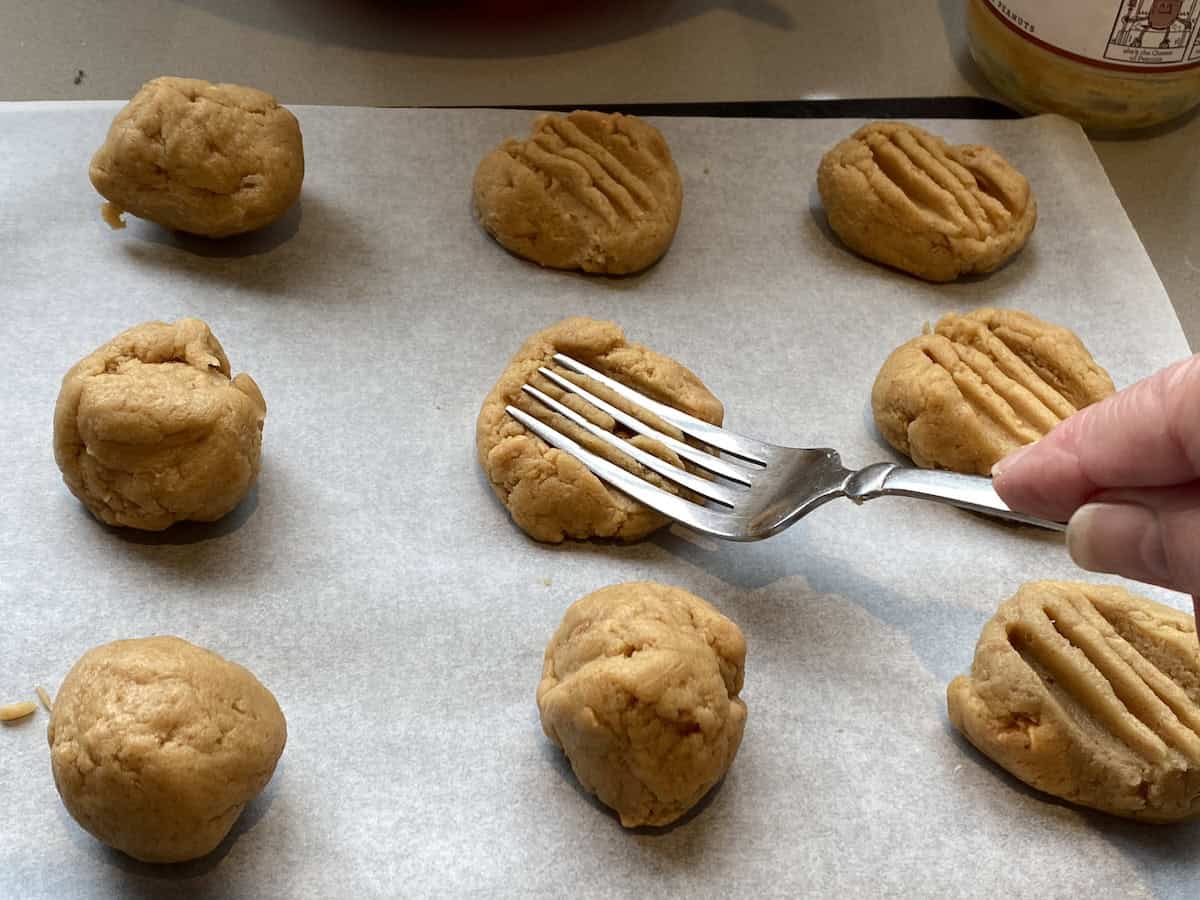 Unbaked Peanut Butter cookie dough on a baking tray, being flattened by a fork.