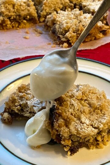 Mincemeat Crumble Traybake with a spoon pouring yogurt on the top.