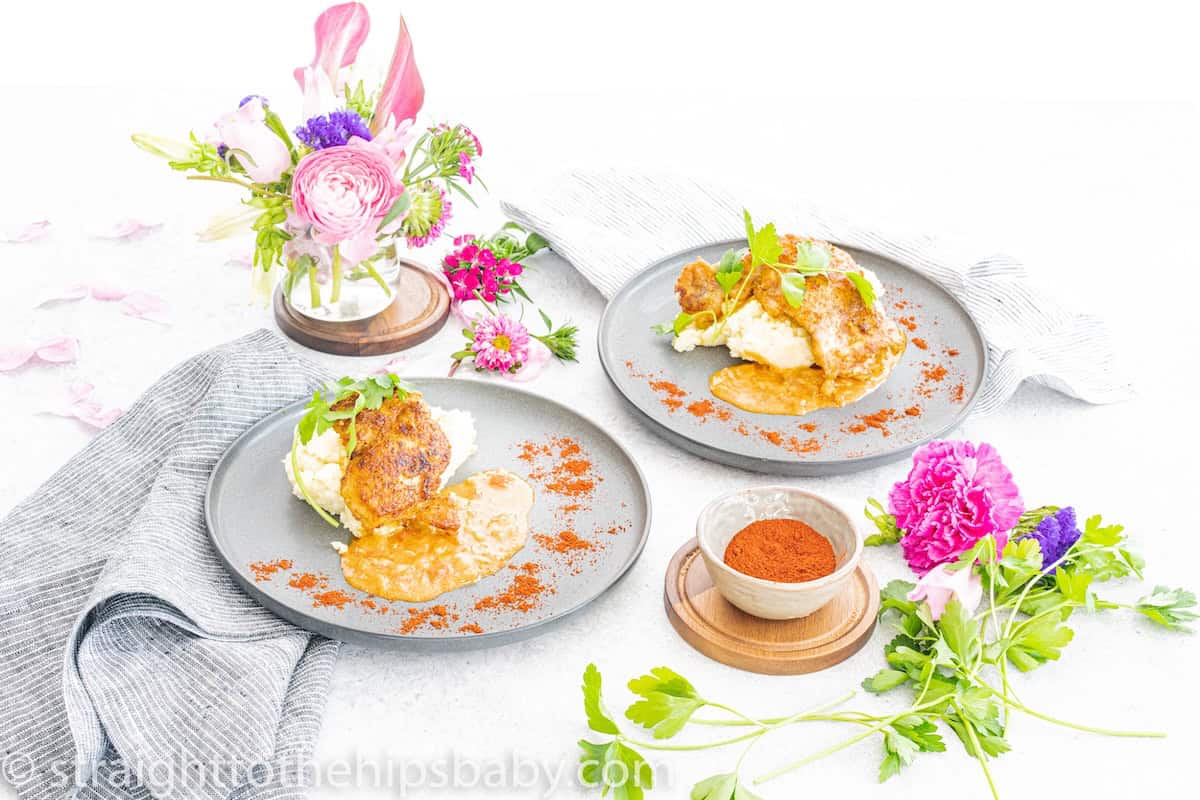 Food on light grey plates with flowers displayed in a glass on the side of the table. Plates of Quick Chicken Paprikash by Jessie Sierra Ross