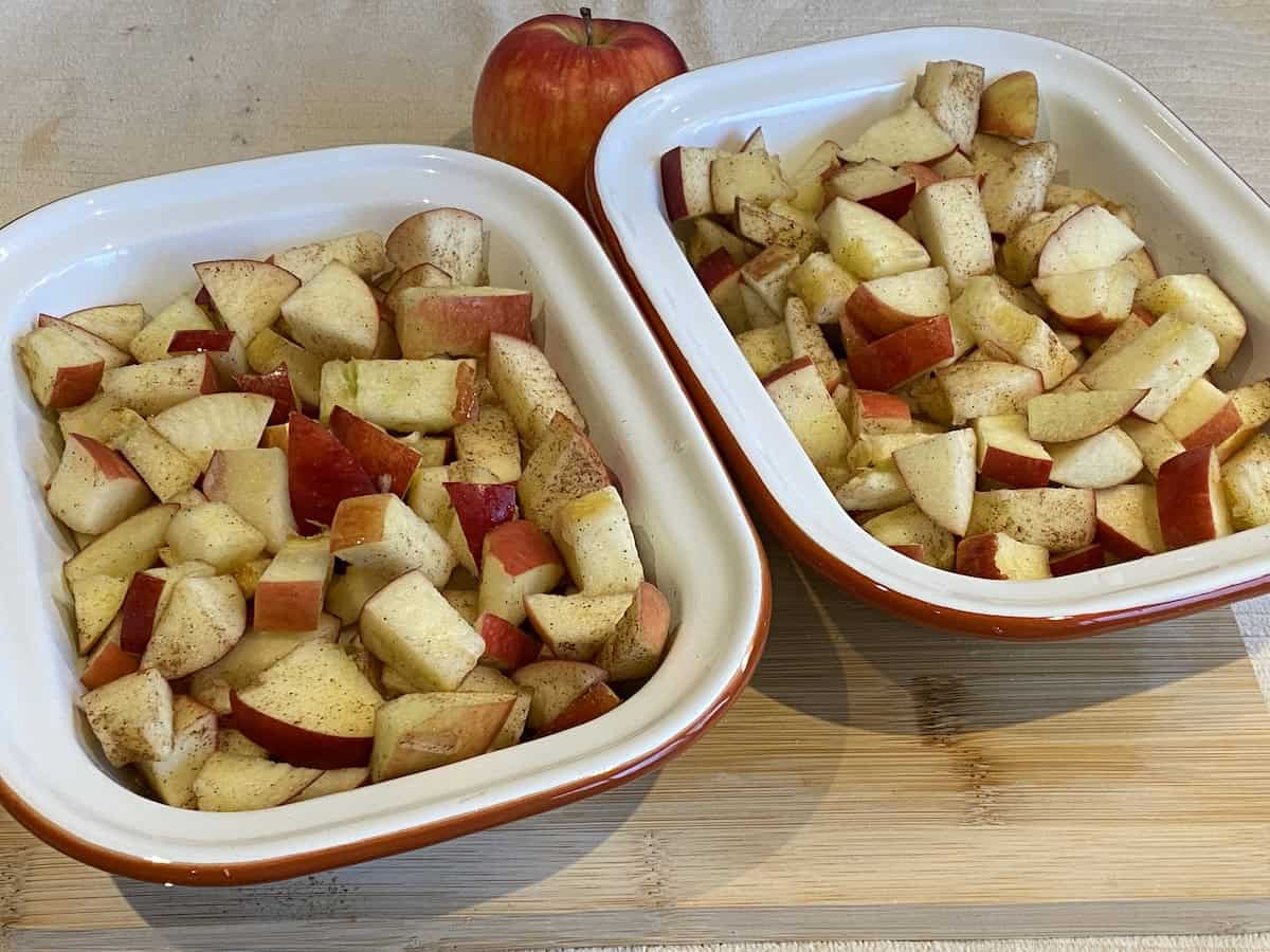 Chunks of apples in tin baking dishes coated in cinnamon.