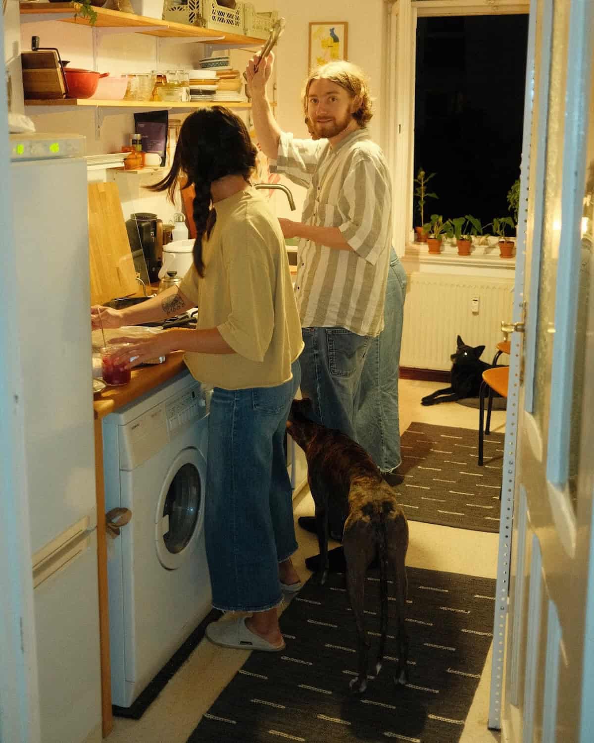 People stood in a kitchen. Devan's kitchen with two people by the counter tops.