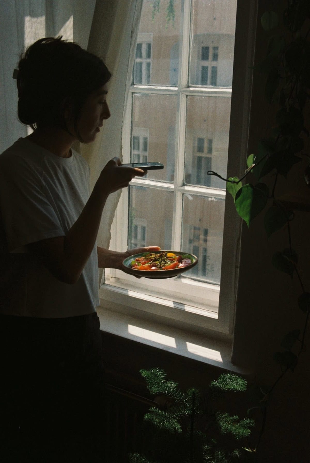 Devan by the window holding a plate of food while taking a picture. Devan by a window holding food in a pan while taking a photo.