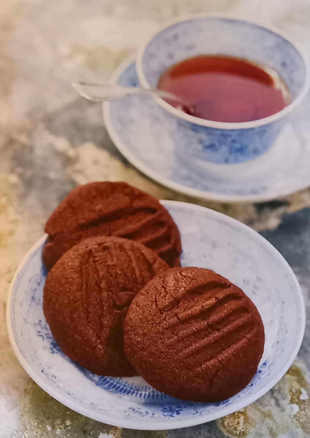 Chocolate cookies on a small white plate, with a cup of tea on the side.