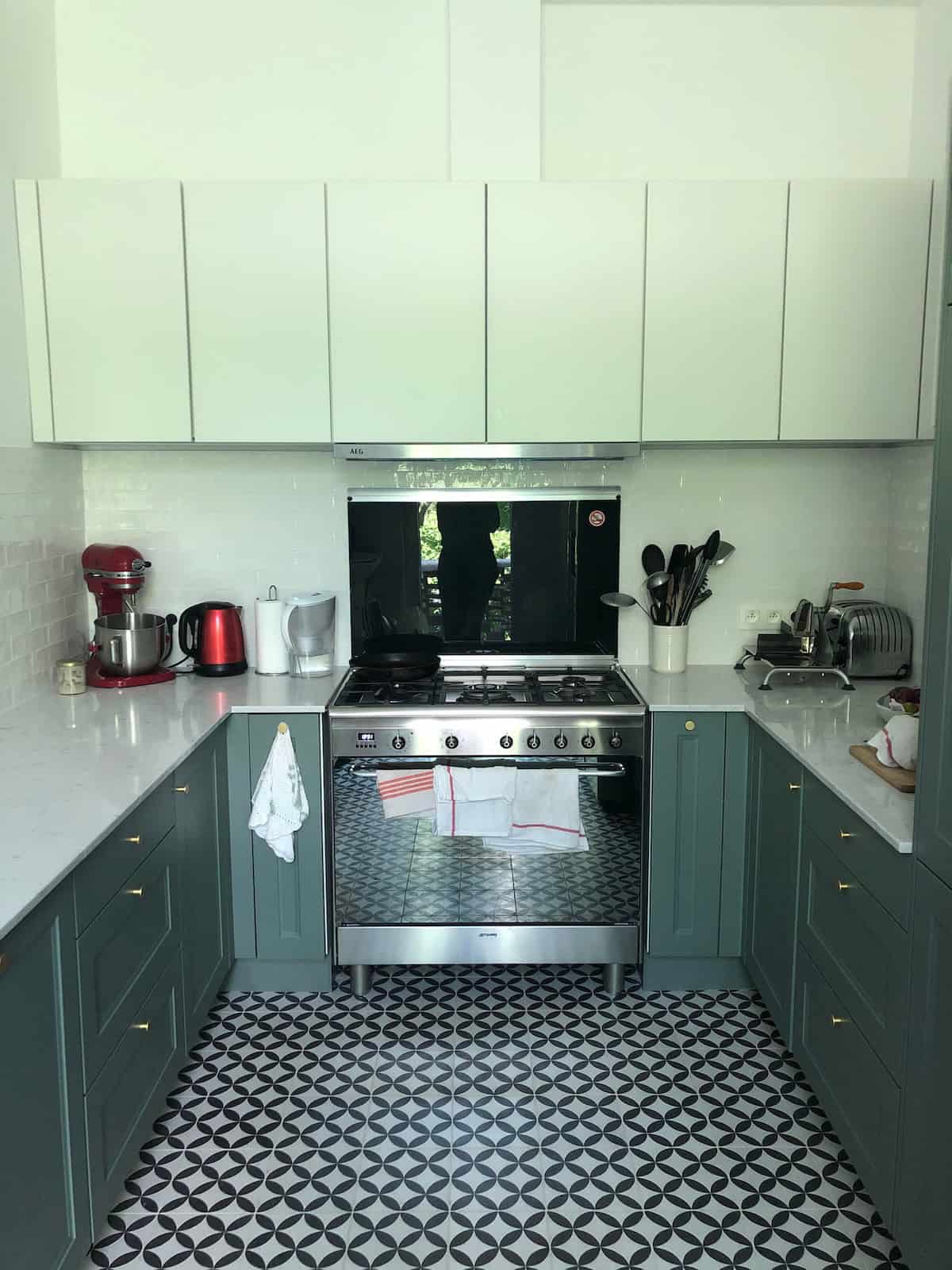 Bright mint green kitchen with grey coloured cupboards and large stove. Sophia's kitchen after renovation. There are cupboards and counter tops on both sides with a large cooker and oven by the back wall with cupboards above it.
