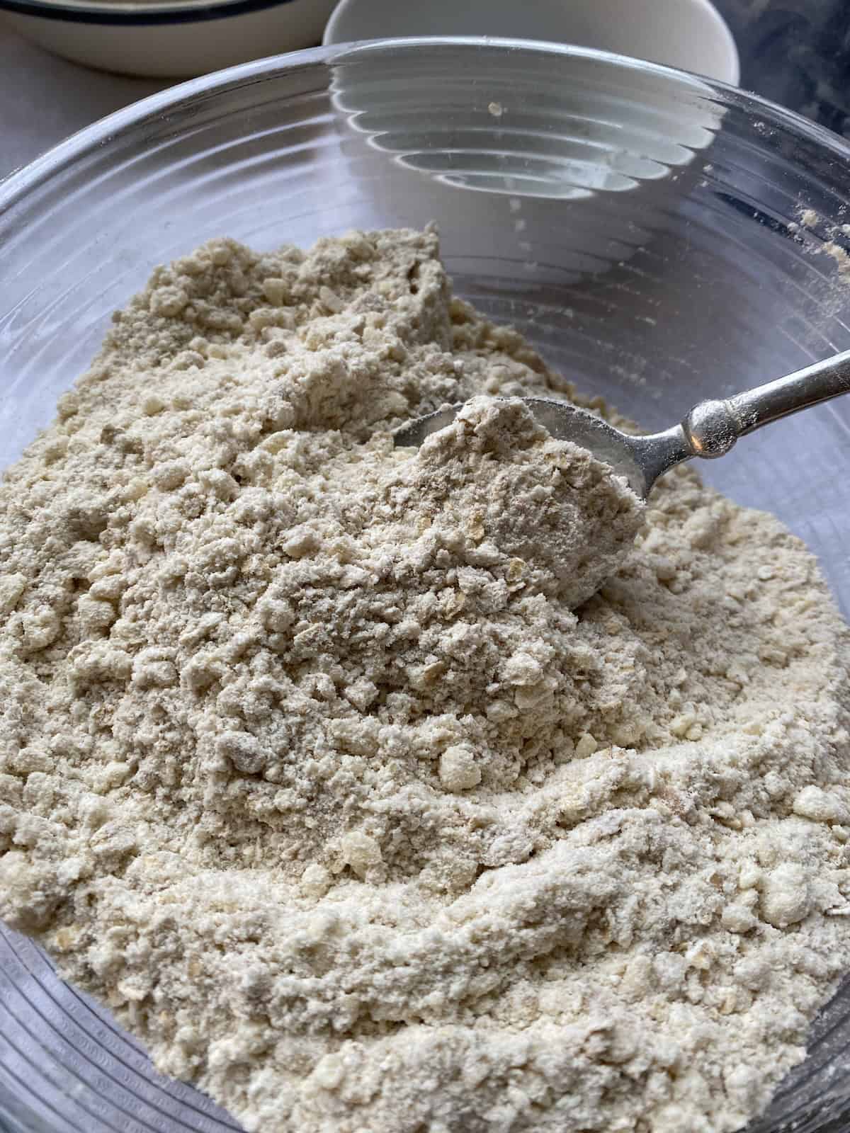 Crumble topping with oats and nuts in a large mixing bowl being mixed with a spoon.