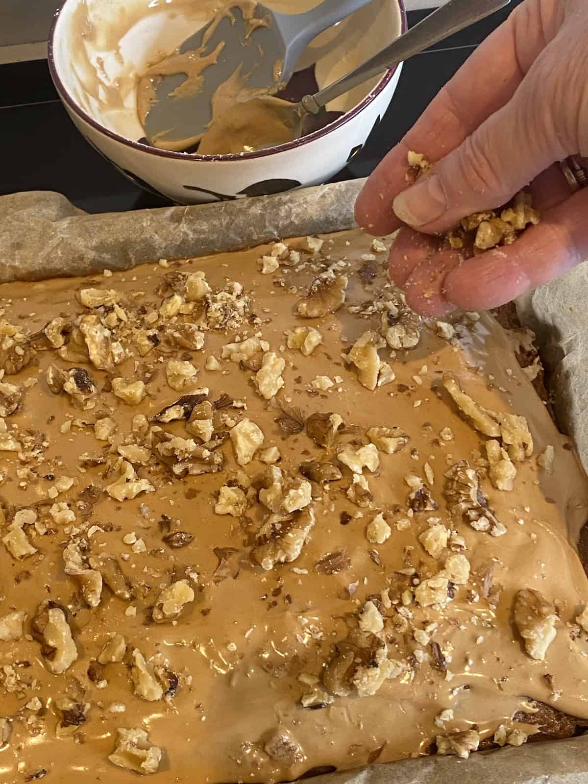 Sprinkling nuts on the top of a coffee and walnut traybake.
