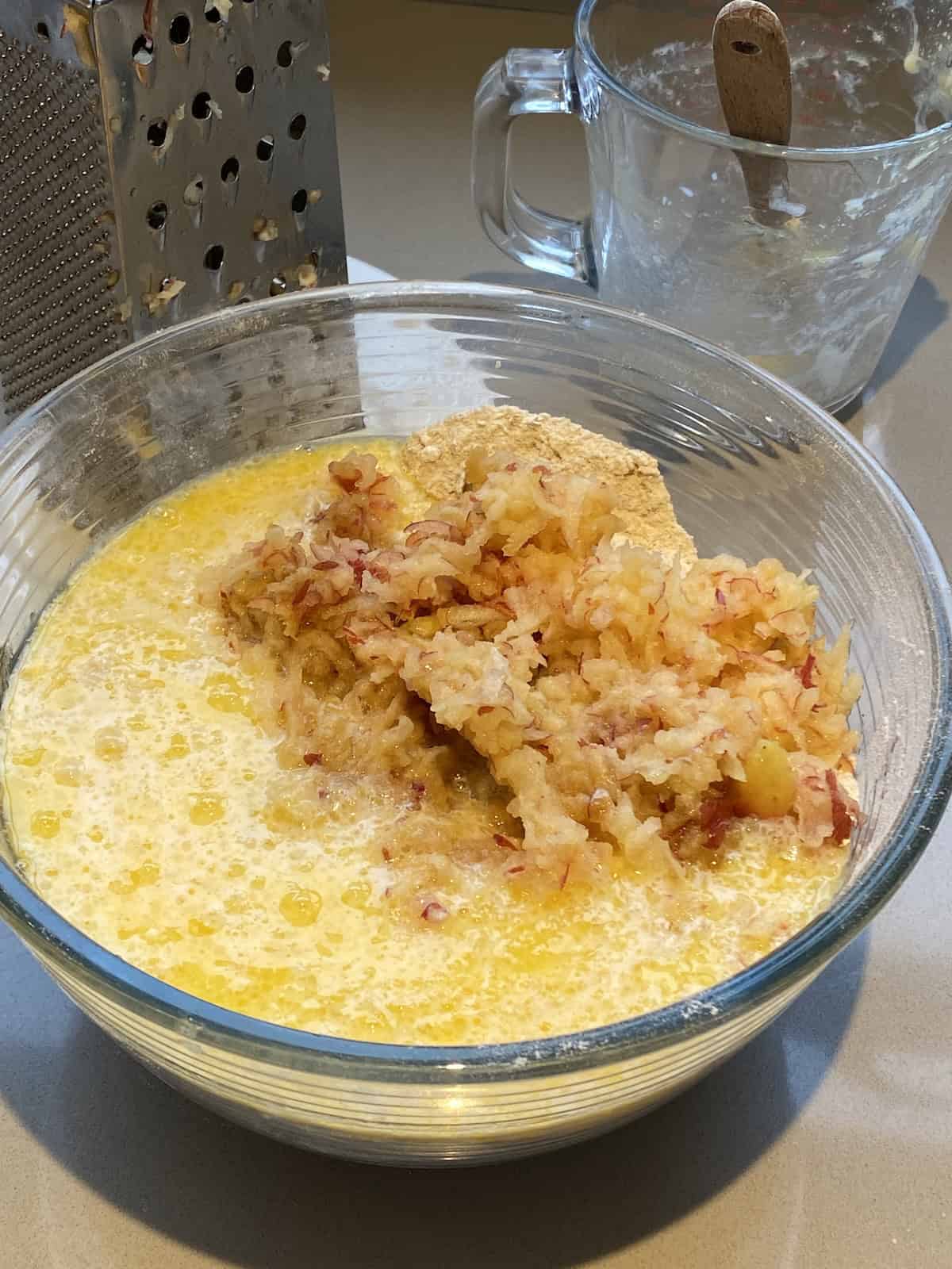Grated apples and muffin batter in a large glass bowl.