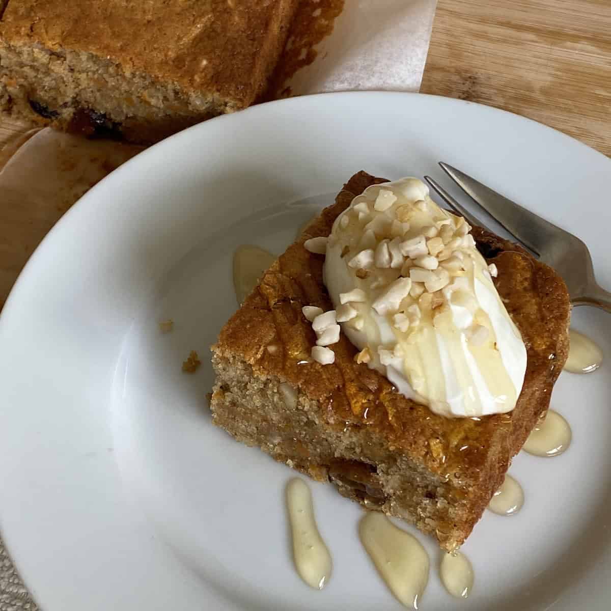 Slice of Carrot Cake Traybake topped with yogurt, honey and nuts.