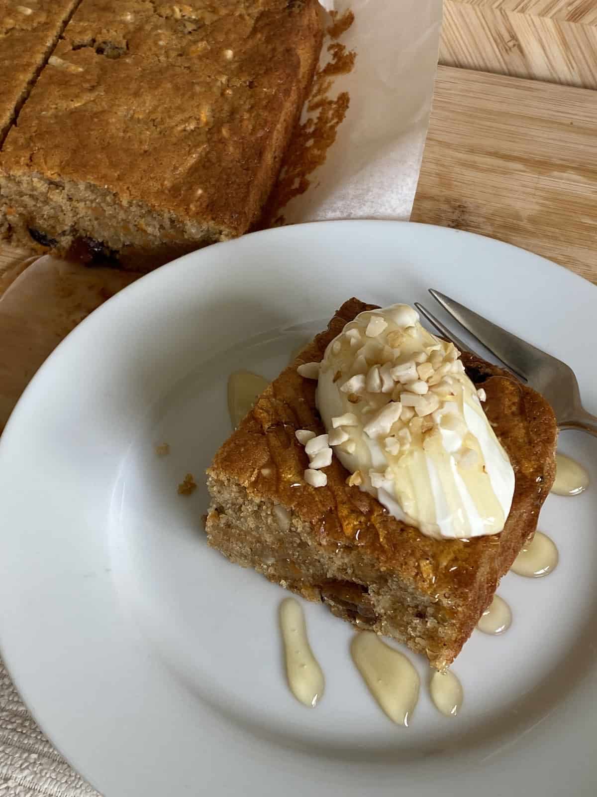 Slice of Carrot Cake Traybake topped with yogurt, honey and nuts.
